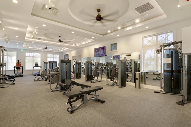 gym with a raised ceiling, visible vents, ceiling fan, and light carpet