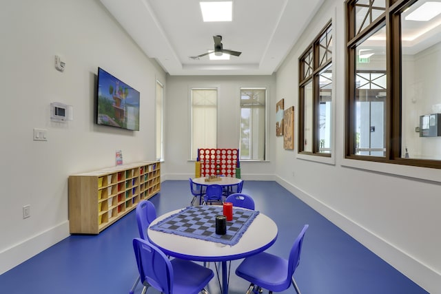 rec room with ceiling fan, a raised ceiling, and baseboards