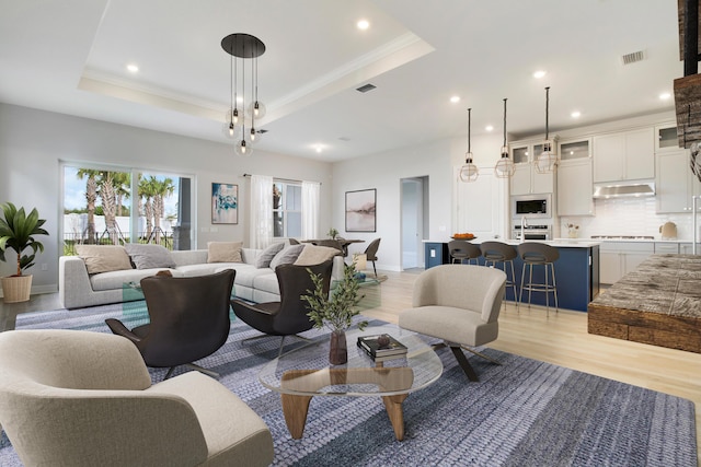 living room with a raised ceiling, visible vents, and light wood-style floors