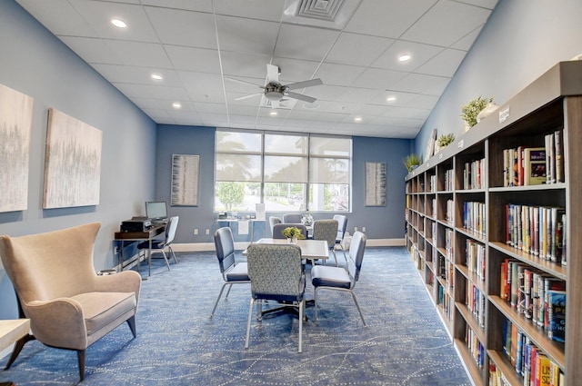 home office featuring bookshelves, dark carpet, visible vents, a ceiling fan, and baseboards