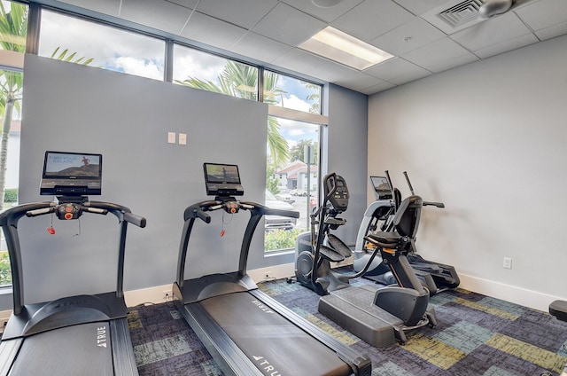 gym with a wall of windows, a paneled ceiling, visible vents, and baseboards