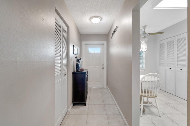 doorway with a ceiling fan, a healthy amount of sunlight, a textured ceiling, and light tile patterned floors