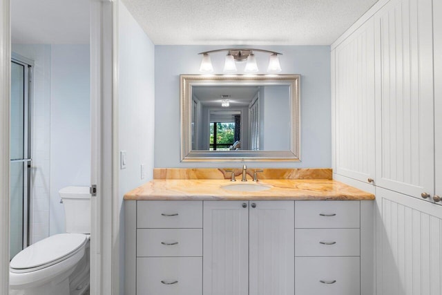 bathroom featuring vanity, a textured ceiling, toilet, and walk in shower