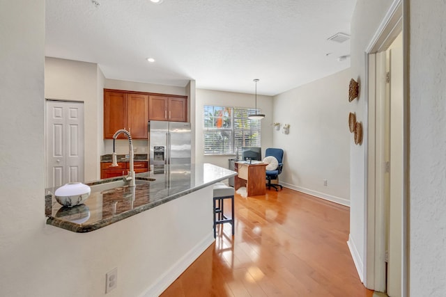 kitchen featuring pendant lighting, sink, a kitchen breakfast bar, stainless steel refrigerator with ice dispenser, and dark stone counters