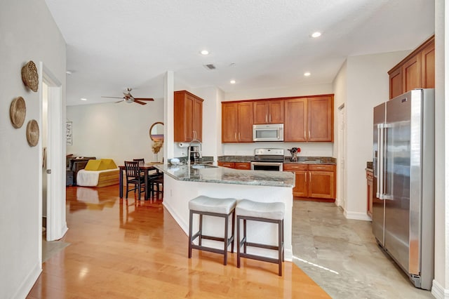 kitchen featuring sink, a breakfast bar, stainless steel appliances, kitchen peninsula, and dark stone counters