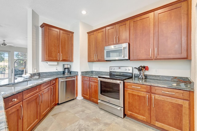 kitchen with dark stone countertops, sink, stainless steel appliances, and ceiling fan