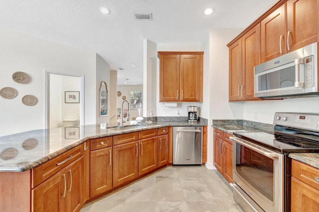 kitchen with sink, stainless steel appliances, light stone countertops, a textured ceiling, and kitchen peninsula