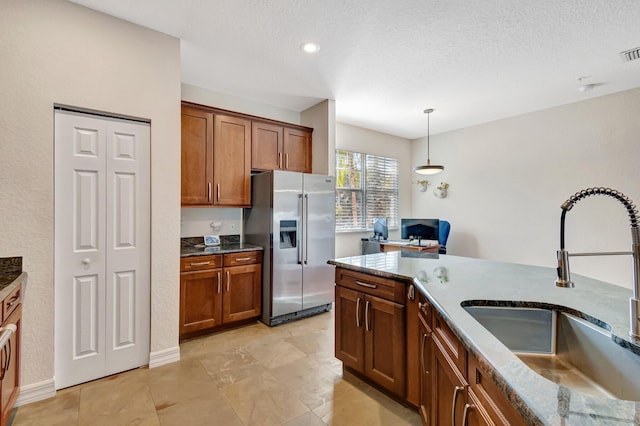 kitchen with sink, high end fridge, light stone countertops, a textured ceiling, and decorative light fixtures