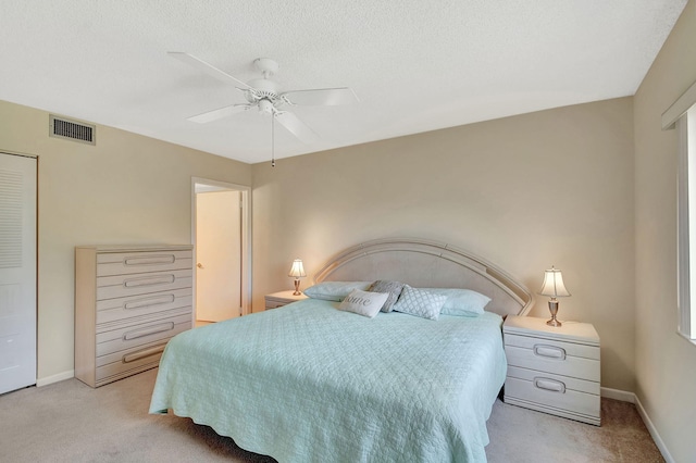 bedroom with ceiling fan, light colored carpet, and a textured ceiling