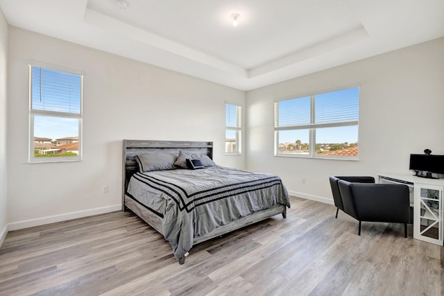 bedroom featuring light wood-type flooring, a raised ceiling, and baseboards