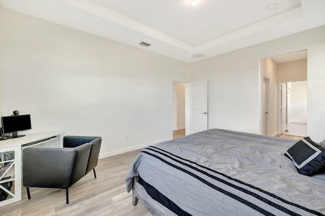 bedroom with light wood-type flooring, baseboards, visible vents, and a tray ceiling