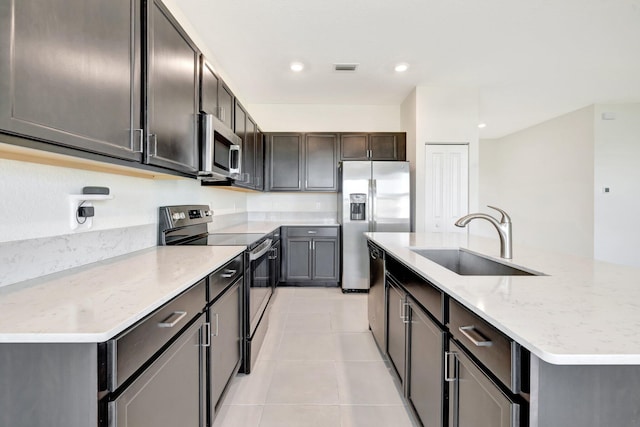 12521 NW Lynch Ln, Port Saint Lucie, FL 34987 - kitchen featuring a sink, stainless steel appliances, light stone counters, a center island with sink, and light tile patterned floors