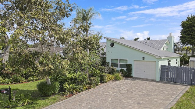 10174 Dogwood Ave, Palm Beach Gardens, FL 33410 - view of property exterior featuring a garage, stucco siding, decorative driveway, fence, and a chimney