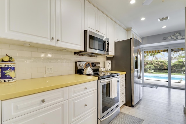10174 Dogwood Ave, Palm Beach Gardens, FL 33410 - kitchen with stainless steel appliances, decorative backsplash, white cabinetry, light wood-type flooring, and light countertops