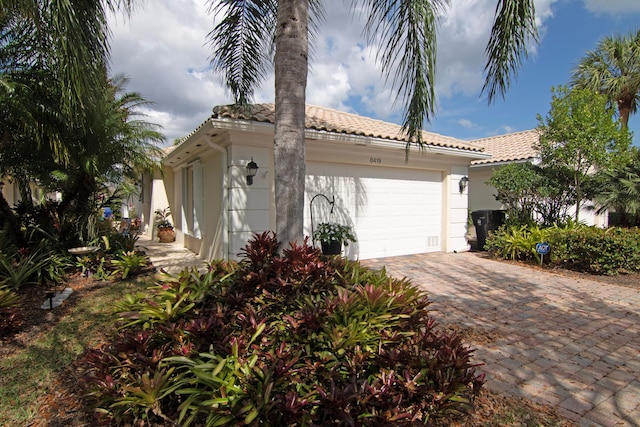 view of side of home with decorative driveway, a tiled roof, an attached garage, and stucco siding