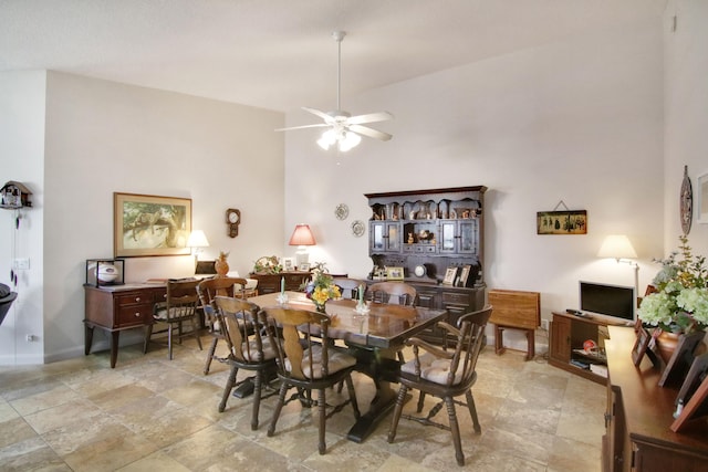 dining space with a ceiling fan, baseboards, and a high ceiling