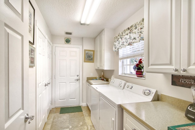 washroom with a textured ceiling, a sink, visible vents, washer and dryer, and cabinet space