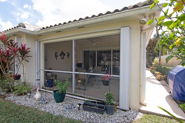 property entrance with ceiling fan, fence, a tile roof, and stucco siding