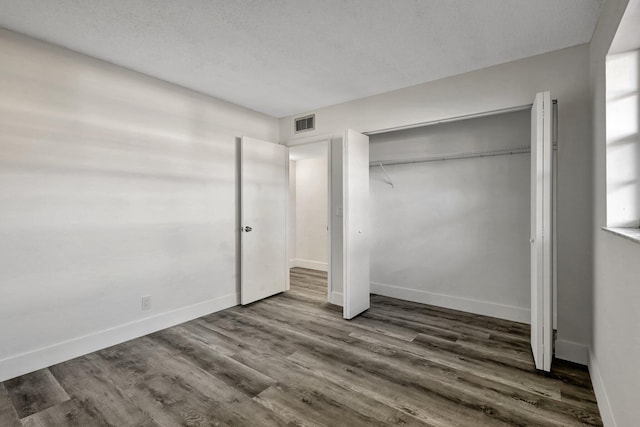 unfurnished bedroom with dark wood-type flooring, a textured ceiling, and a closet