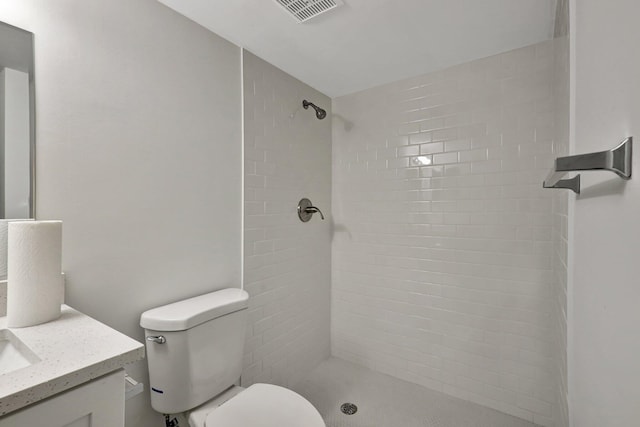 bathroom featuring vanity, a tile shower, and toilet