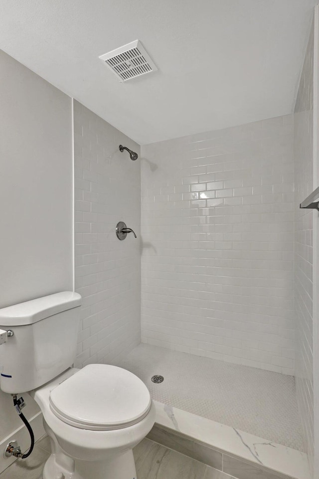 bathroom with a tile shower and toilet