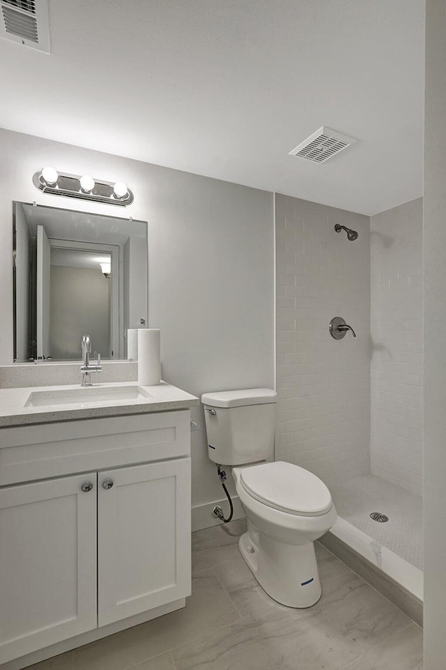 bathroom with tiled shower, vanity, and toilet