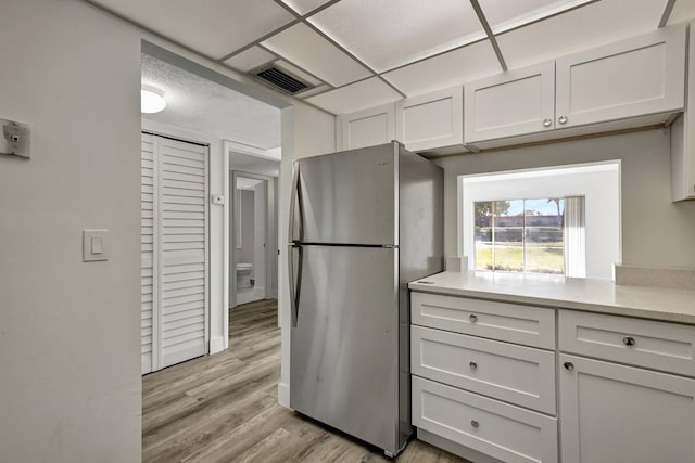 kitchen with light hardwood / wood-style flooring, stainless steel refrigerator, and white cabinets