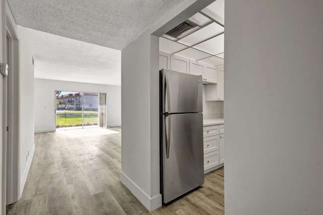 kitchen with stainless steel refrigerator, a textured ceiling, light hardwood / wood-style flooring, and white cabinets