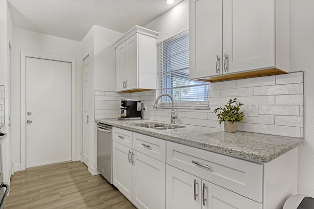 kitchen featuring light stone counters, sink, stainless steel dishwasher, and white cabinets