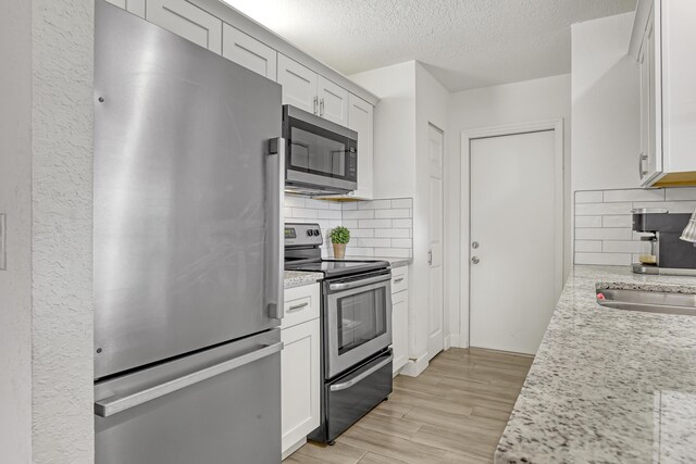 kitchen featuring white cabinetry, light stone countertops, light hardwood / wood-style floors, and appliances with stainless steel finishes