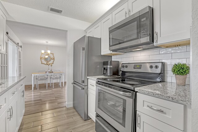 kitchen featuring white cabinetry, tasteful backsplash, appliances with stainless steel finishes, light stone countertops, and light hardwood / wood-style floors