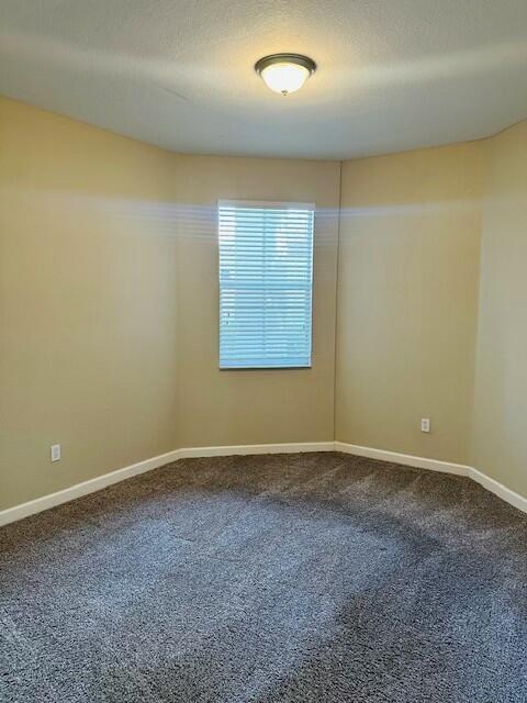 unfurnished room featuring a textured ceiling, dark colored carpet, and baseboards