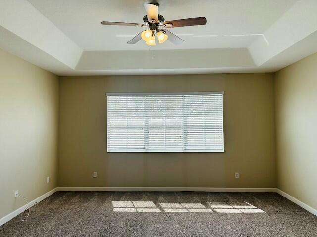 empty room with carpet floors, baseboards, and a raised ceiling