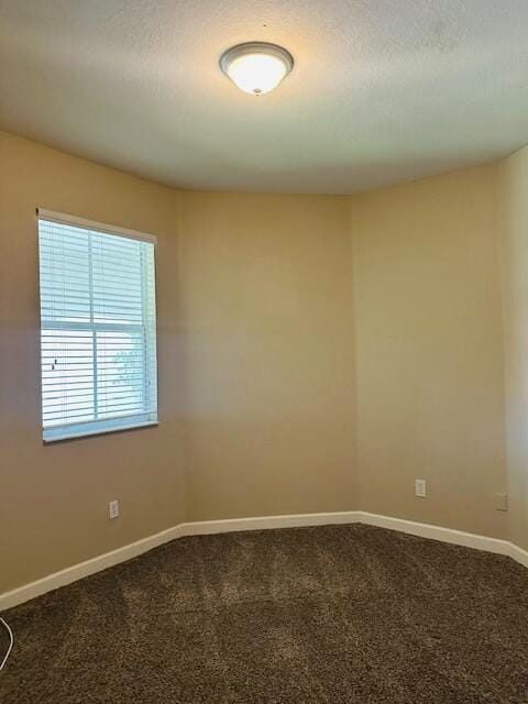 empty room with baseboards, dark colored carpet, and a textured ceiling