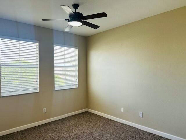 unfurnished room with dark colored carpet, a ceiling fan, and baseboards