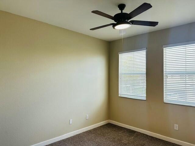 spare room featuring a ceiling fan, dark carpet, and baseboards