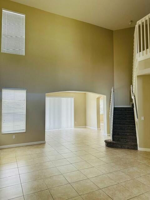 unfurnished living room with light tile patterned floors, baseboards, stairs, and a high ceiling