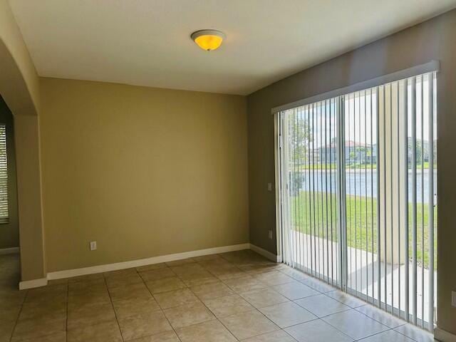 empty room featuring arched walkways, light tile patterned flooring, and baseboards