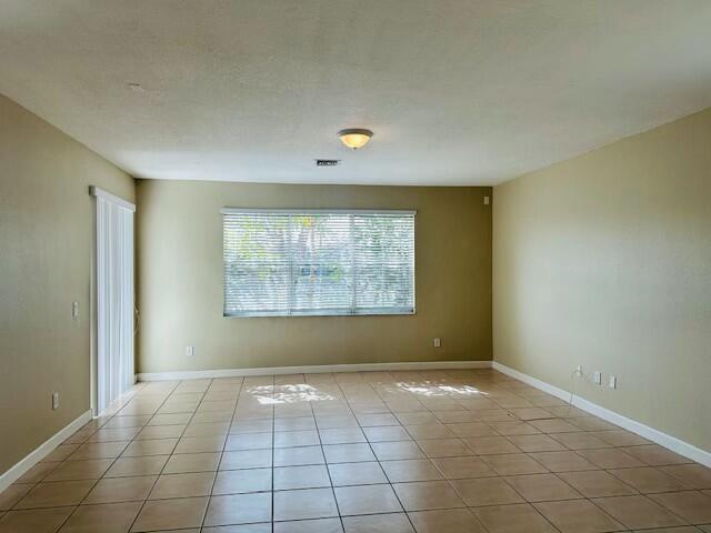 spare room featuring light tile patterned floors, baseboards, visible vents, and a textured ceiling