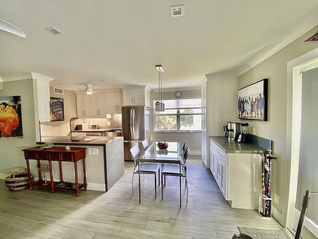 kitchen featuring a breakfast bar, stainless steel refrigerator, white cabinets, hanging light fixtures, and ceiling fan