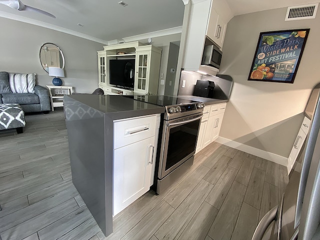 kitchen with crown molding, kitchen peninsula, white cabinets, and appliances with stainless steel finishes