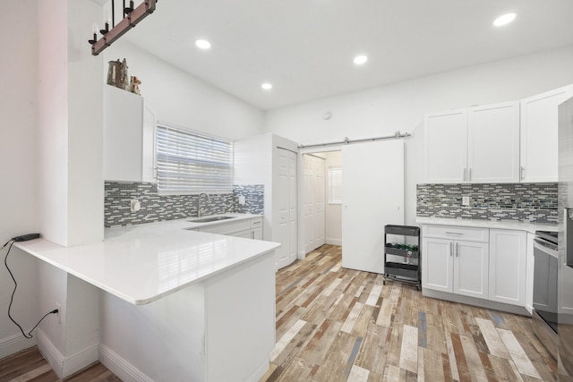 331 NW 1st Ave, Boynton Beach, FL 33435 - kitchen featuring sink, light hardwood / wood-style flooring, kitchen peninsula, a barn door, and white cabinets