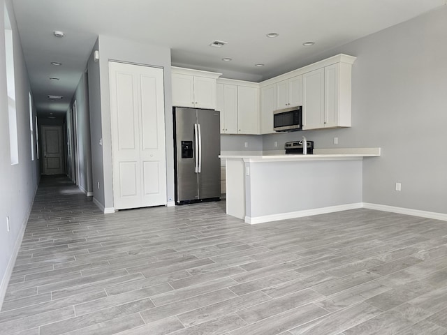 kitchen with stainless steel appliances, white cabinets, light wood-type flooring, and kitchen peninsula