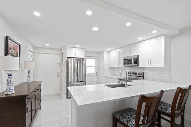 kitchen featuring a breakfast bar, appliances with stainless steel finishes, backsplash, white cabinets, and kitchen peninsula