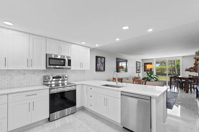 kitchen with appliances with stainless steel finishes, tasteful backsplash, white cabinetry, sink, and kitchen peninsula