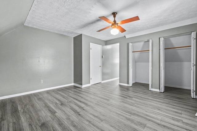 unfurnished bedroom featuring a textured ceiling, two closets, baseboards, and wood finished floors