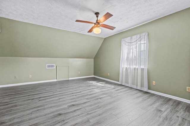 additional living space featuring a textured ceiling, lofted ceiling, light wood-style flooring, visible vents, and a ceiling fan