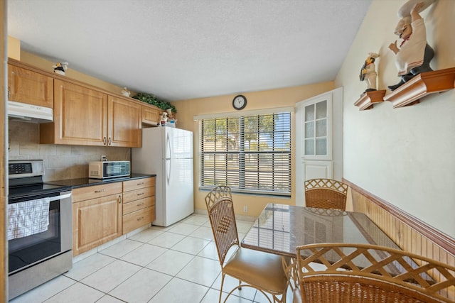 kitchen featuring stainless steel electric range oven, wooden walls, white fridge, light tile patterned floors, and light brown cabinets