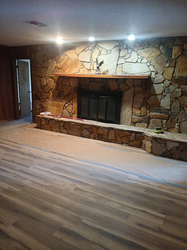 interior details featuring hardwood / wood-style flooring, a stone fireplace, and a textured ceiling