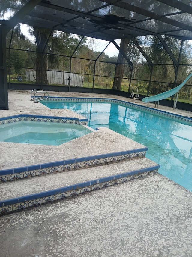 view of pool with a patio area, glass enclosure, and a water slide